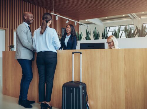 Two Smiling Guests Checking In At A Hotel Reception